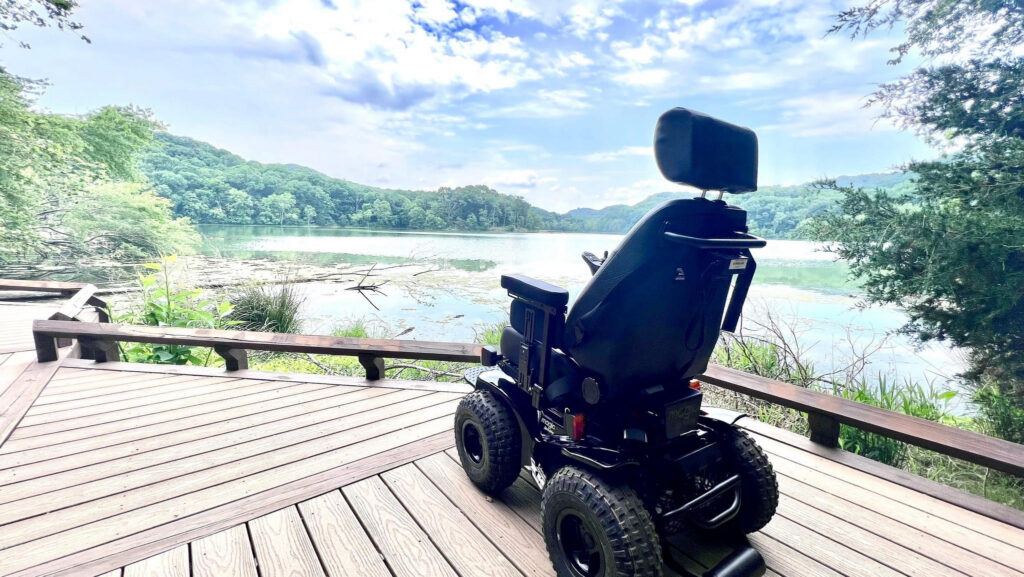 Powered wheelchair on a lakeside deck with forested hills in the background
